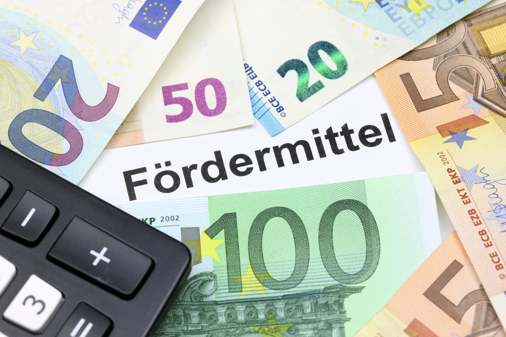 Das Bild zeigt den Schriftzug "Fördermittel". Dieser ist umgeben von EURO-Banknoten und einem Taschenrechner