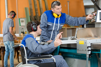 Das Bild zeigt einen Arbeitnehmer im Rollstuhl und einen Arbeitnehmer, der daneben steht.